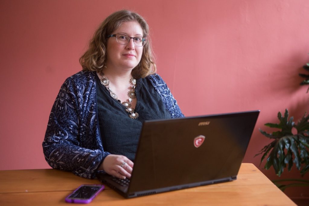 Lindley, a body liberation and positivity activist, sits at her laptop in a room with pink walls.