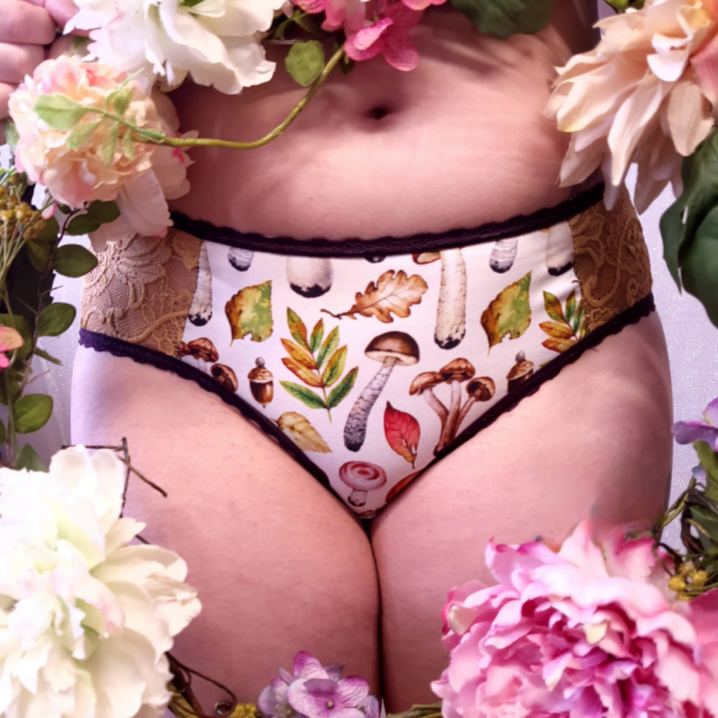Image description: Flowers and leaves in the foreground of picture person wearing underwear with lace insets and mushroom print
