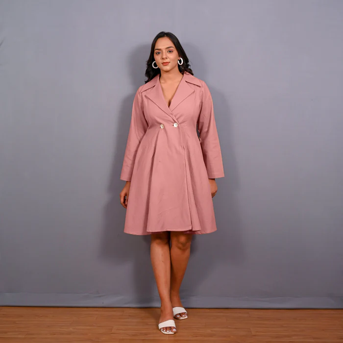 Image description: A person wearing a pink coatdress stands in front of a gray background