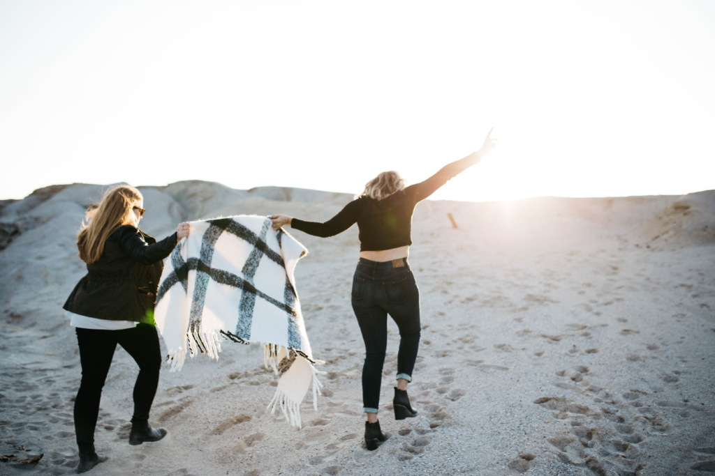 Two women on a sand dune facing the sunrise with their hands uplifted