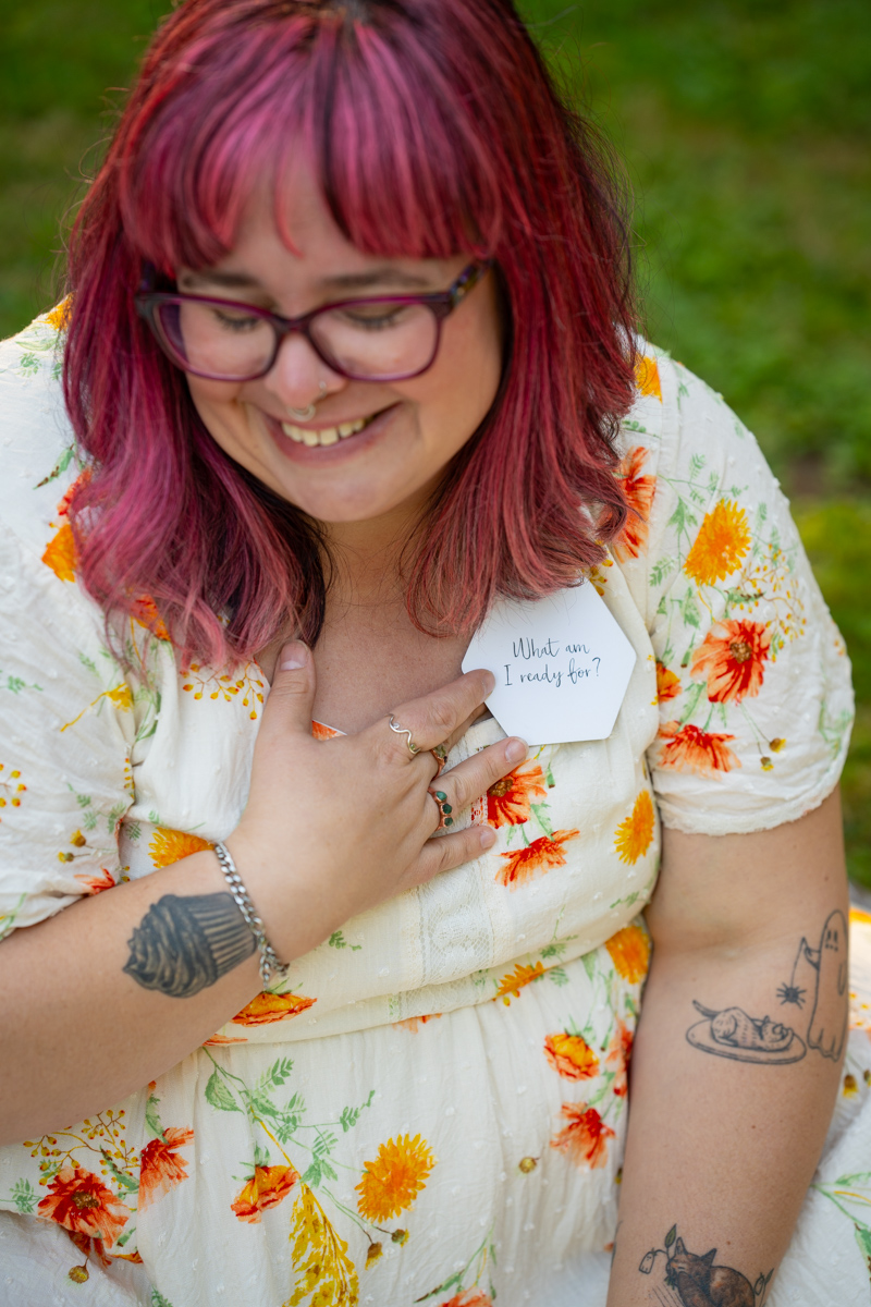 A woman at a photo shoot focused on body image and eating disorder recovery holds a journaling prompt card to her chest in a park.