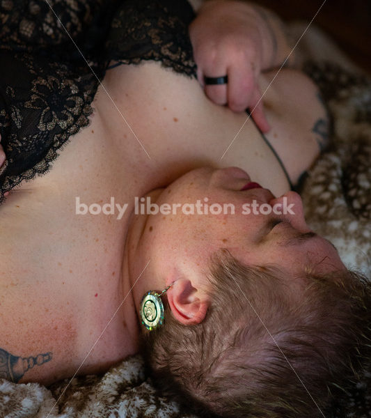 Body Positive Stock Photo: A Plus Size Woman Laying on Soft Blankets in a Negligee Looking Down at Her Body - Body Liberation Photos