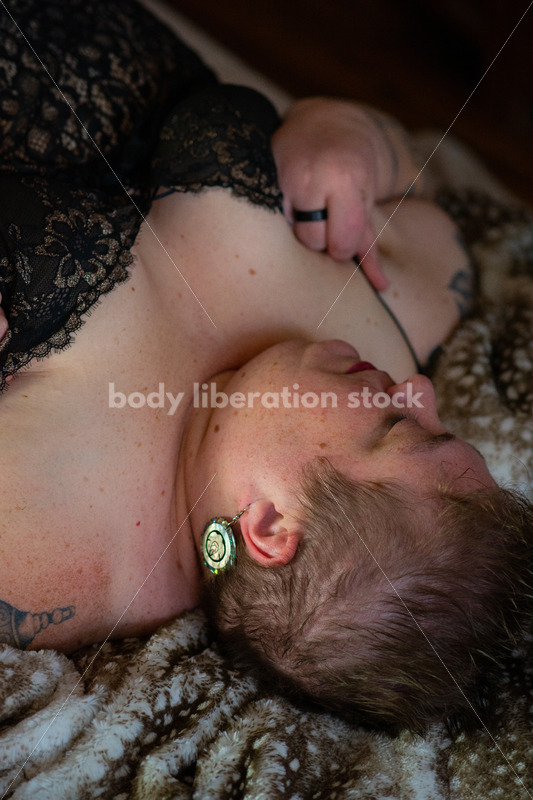 Body Positive Stock Photo: A Plus Size Woman Laying on Soft Blankets in a Negligee Looking Down at Her Body - Body Liberation Photos