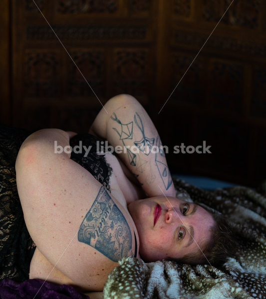 Body-Positive Stock Photo: Plus Size Woman Relaxing on Soft Blankets with a Daring Expression - Body Liberation Photos