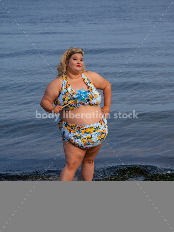Body-Positive Stock Photo: Plus Size Woman in a Blue Swimsuit Posing on the Beach with a Matching Pinwheel - It's time you were seen ⟡ Body Liberation Photos