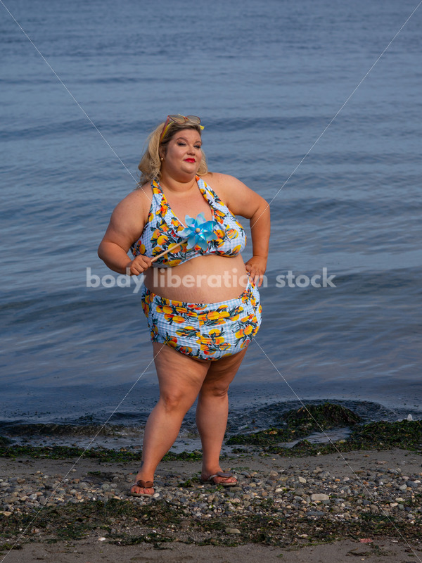 Body-Positive Stock Photo: Plus Size Woman in a Blue Swimsuit Posing on the Beach with a Matching Pinwheel - It's time you were seen ⟡ Body Liberation Photos
