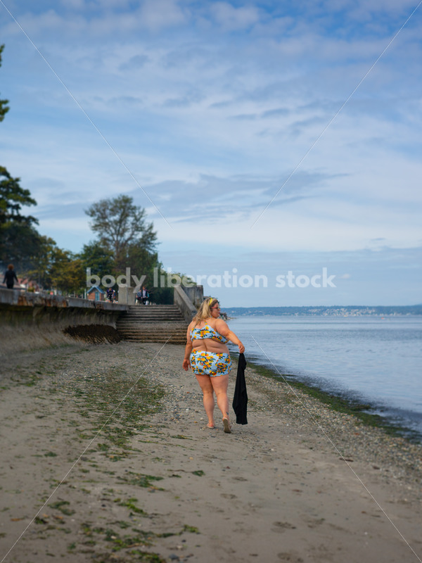 Body-Positive Stock Photo: Plus Size Woman in a Blue Swimsuit Walks Along the Beach Holding a Coverup - It's time you were seen ⟡ Body Liberation Photos