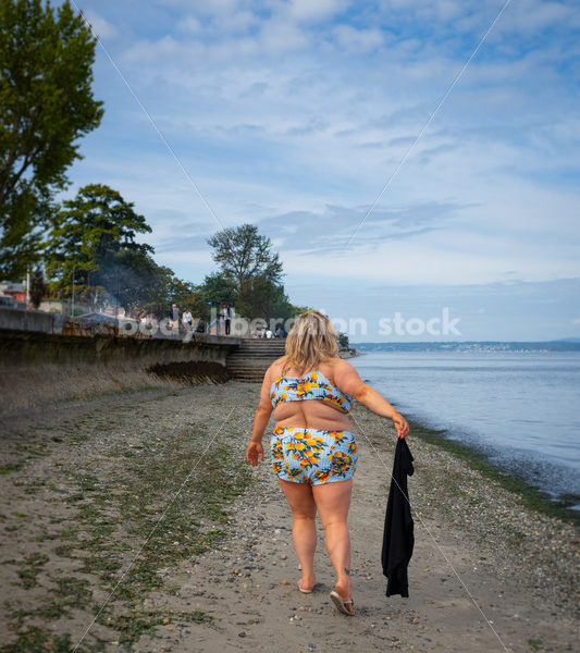 Body-Positive Stock Photo: Plus Size Woman in a Blue Swimsuit Walks Along the Beach Holding a Coverup - Body Liberation Photos & Stock