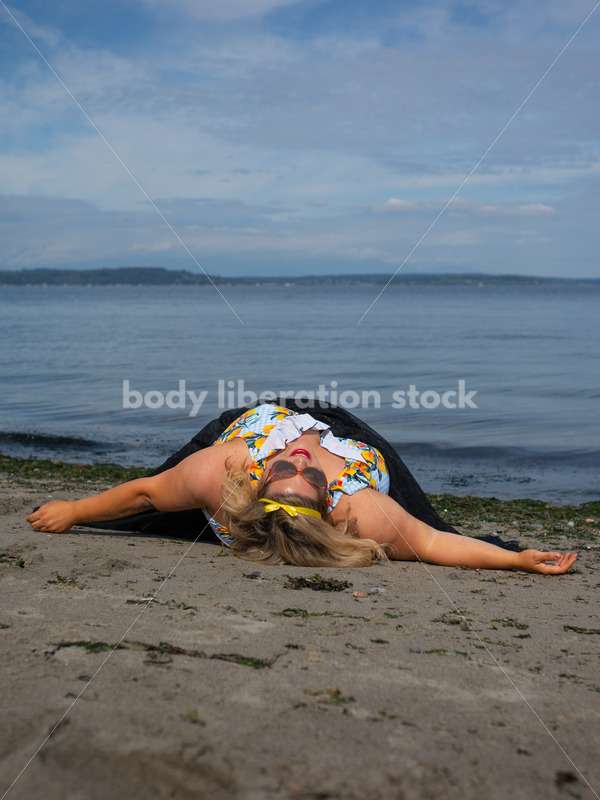 Body-Positive Stock Photo: Plus Size Woman in a Blue Swimsuit and Skirt Coverup Lays on the Sand Laughing - It's time you were seen ⟡ Body Liberation Photos