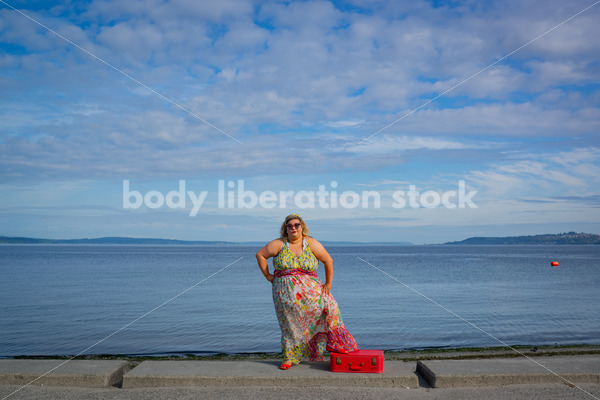 {Fat Glam Summer} Body-Positive Stock Photo: Plus Size Woman Stands by the Ocean with One Foot on a Red Suitcase - Body Liberation Photos & Stock