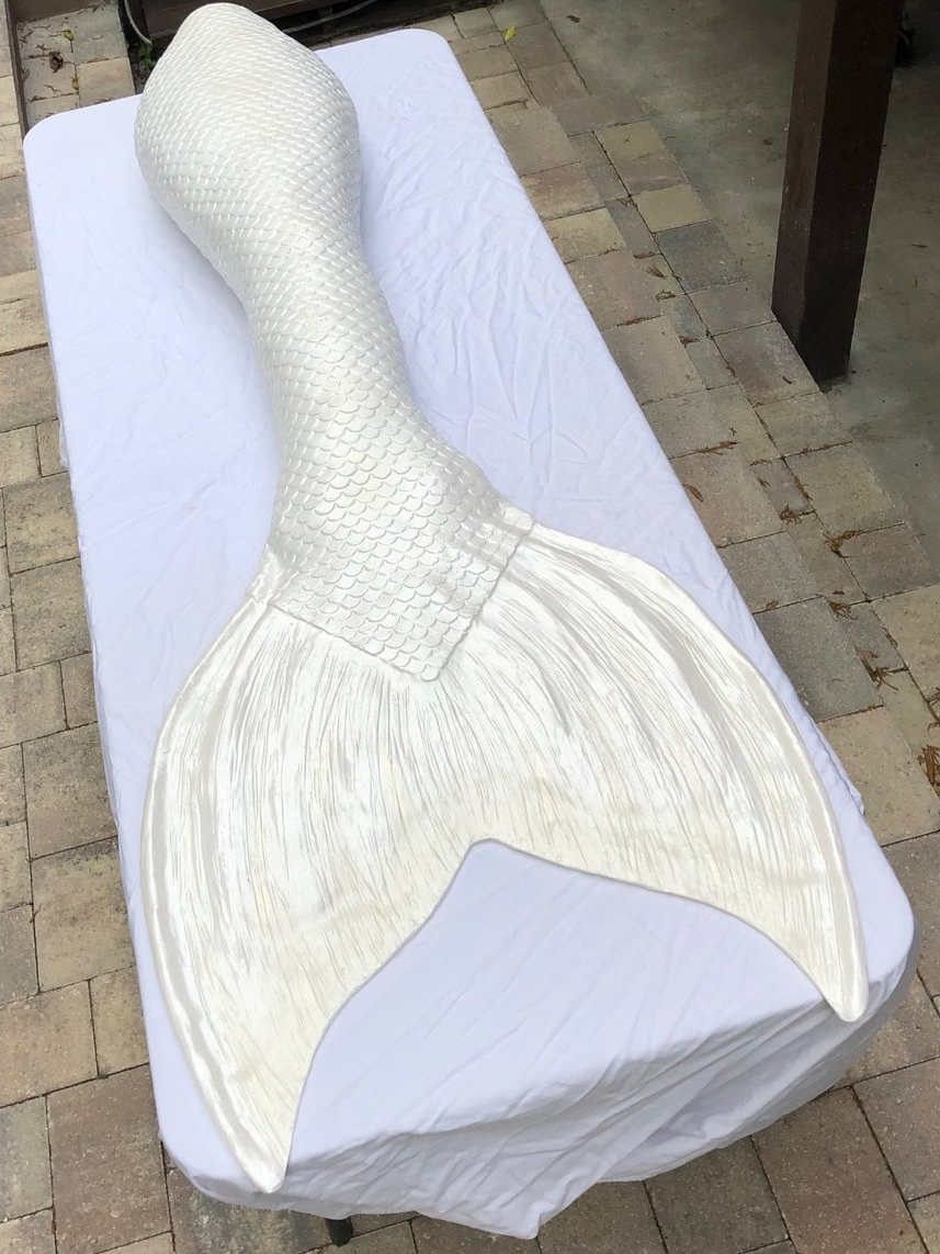 A pearlescent white mermaid tail rests on a table covered in white cloth
