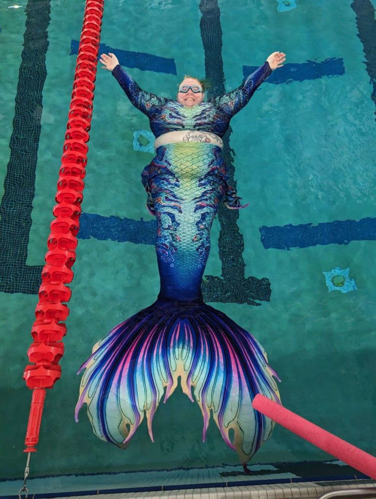 A fat mermaid shows off her tail and top covering in a pool