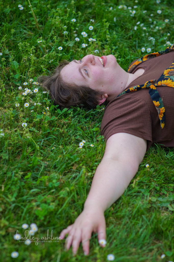 A non-binary person with short hair and casual clothes lies on their back in the grass and gazes up at the sky during a queer-friendly Seattle small business branding photo session for coaches.