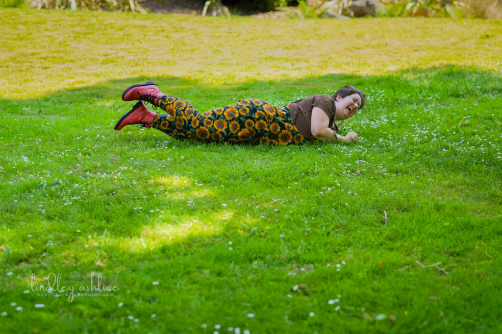 A laughing fat non-binary person rolling down a grassy hill during a queer-friendly, body-positive Seattle business portrait session.