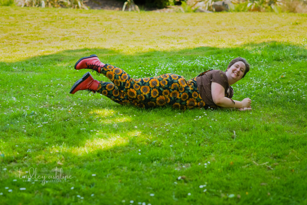 A laughing fat non-binary person rolling down a grassy hill during a queer-friendly, body-positive Seattle business portrait session.