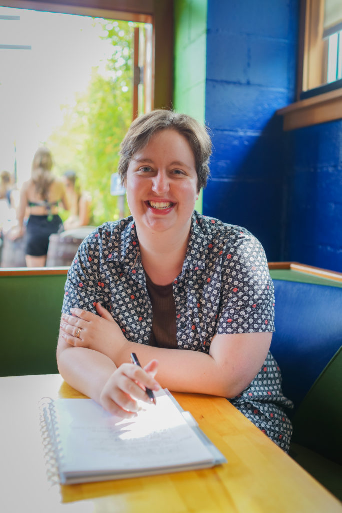 A non-binary person with short hair and casual clothes smiles and takes notes at a restaurant table during a Seattle small business branding photo session for coaches.
