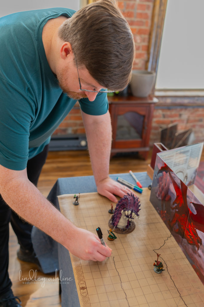 A white man with a D&amp;D DM screen setup draws on a map at a Seattle autism-friendly portrait photo session.