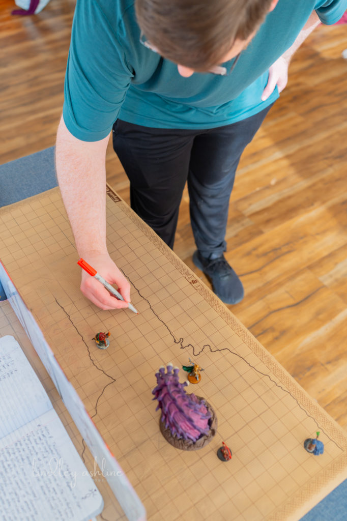 A white man with a D&amp;D DM screen setup draws on a map at a Seattle autism-friendly portrait photo session.