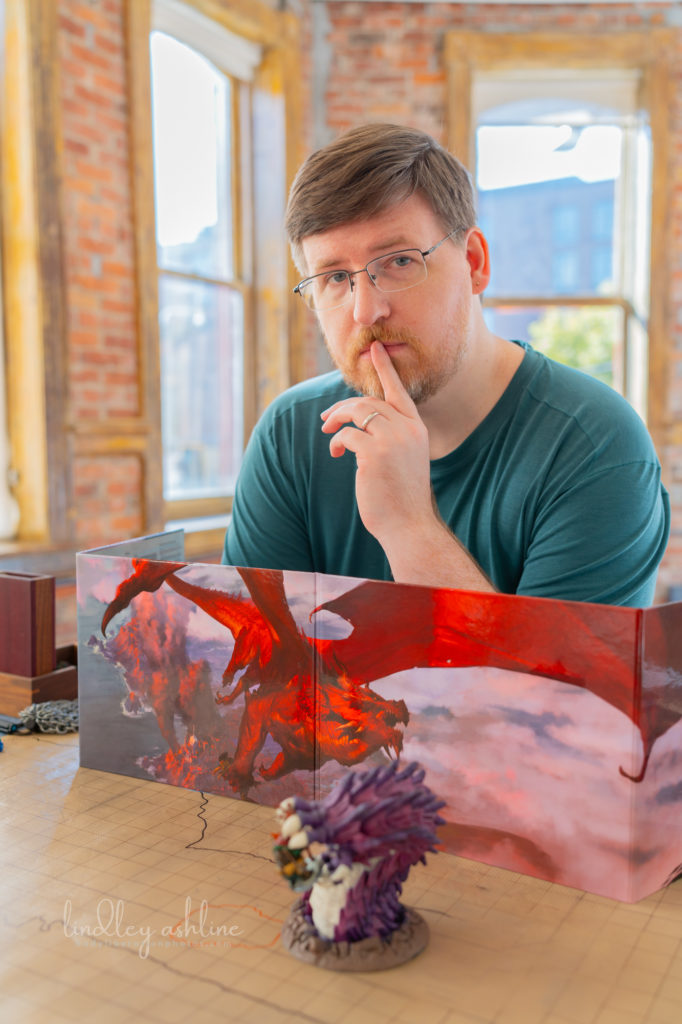 A mid-size white male gamer with a D&amp;D DM screen setup thinks in a sunlit room at a Seattle professional portrait photo session.