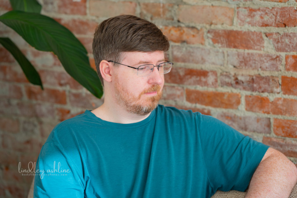 An autistic white man in a t-shirt looks away from the camera with a neutral expression at a Pacific Northwest autism-friendly business branding photo shoot.