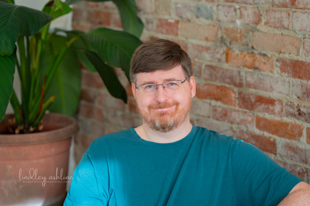 An midsize white man in a t-shirt looks at the camera with a wry expression at a Pacific Northwest autism-friendly business branding photo shoot.