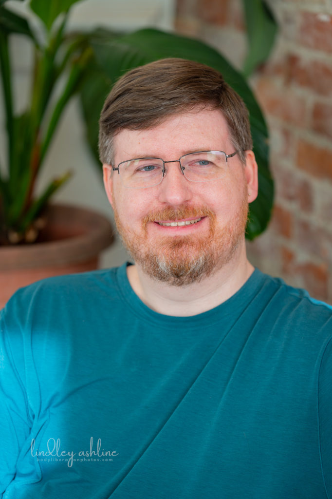 An autistic white man in a t-shirt looks away from the camera with a neutral expression at a Pacific Northwest autism-friendly business branding photo shoot.